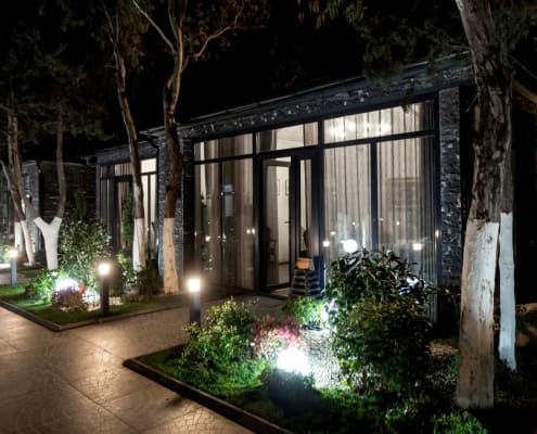 commercial landscape lighting in waco TX Modern building with commercial landscape lighting at night. Path leads to glass doors, surrounded by illuminated greenery. Pressure washing may be needed to maintain the clean look.