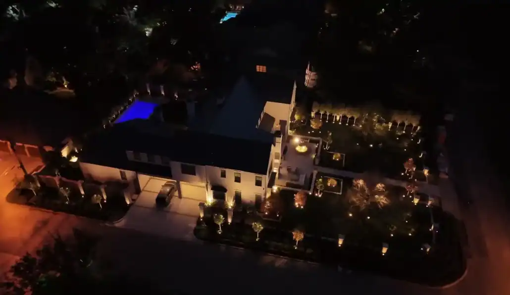 lumos outdoor lighting in Waco TX Aerial view of a luxurious home at night, showcasing elegant outdoor lighting that illuminates the manicured garden and pool area, enhancing the home's curb appeal.