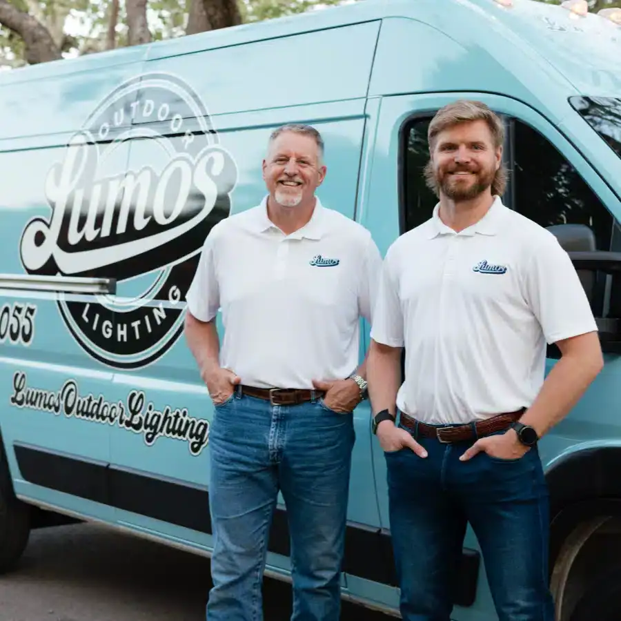 lumos outdoor lighting services in waco 2 Two men from Lumos Outdoor Lighting stand proudly in front of their company van. The light blue van features the Lumos logo. Both men wear white polo shirts and jeans, smiling confidently.