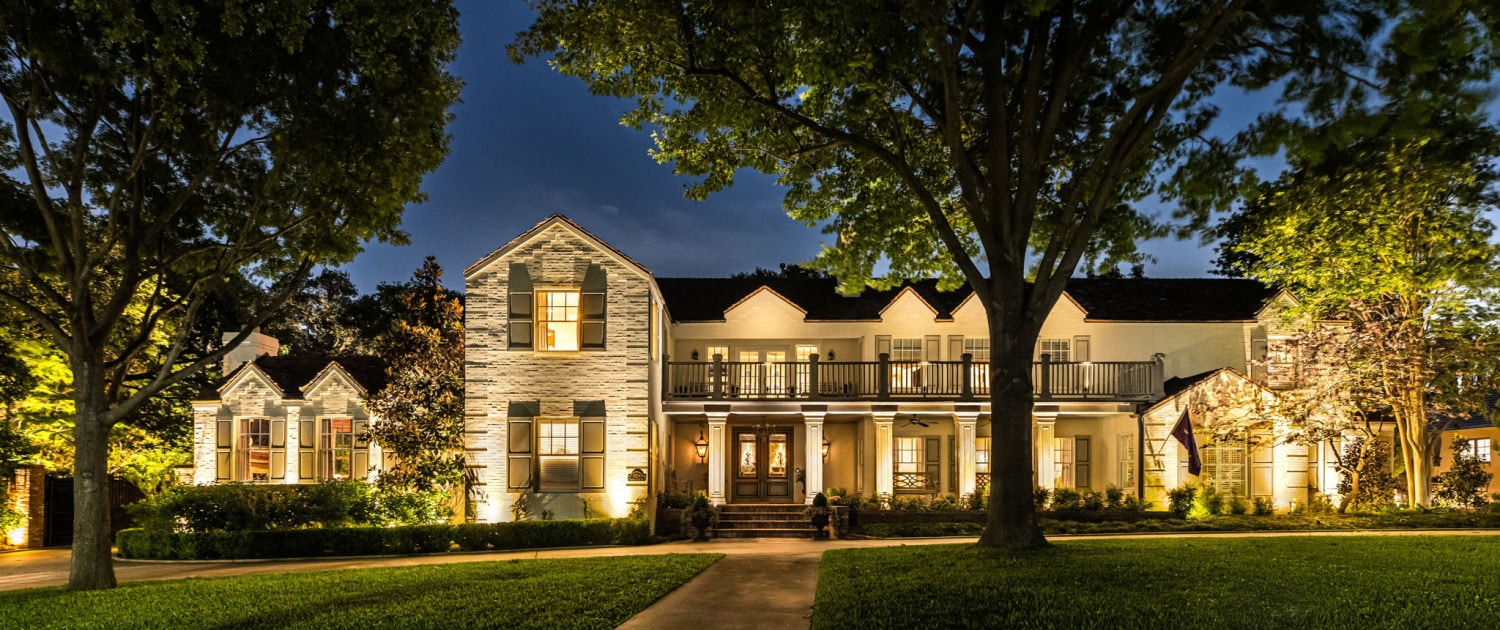 Elegant Home Exterior with Outdoor Lighting Beautifully illuminated large house at night with landscape lighting highlighting trees and facade.