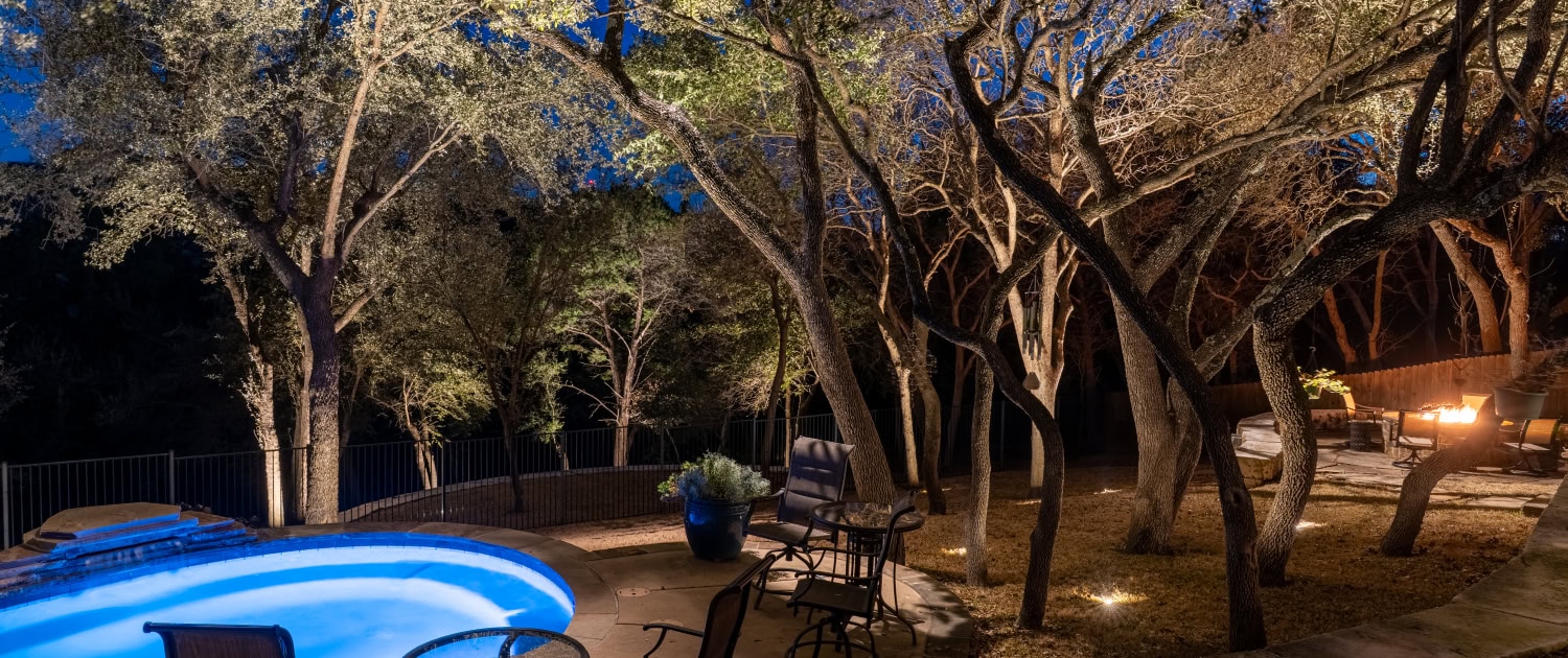 Outdoor Pool Area with Landscape Lighting Beautiful outdoor pool area illuminated with landscape lighting, surrounded by trees and outdoor furniture, perfect for evening relaxation.