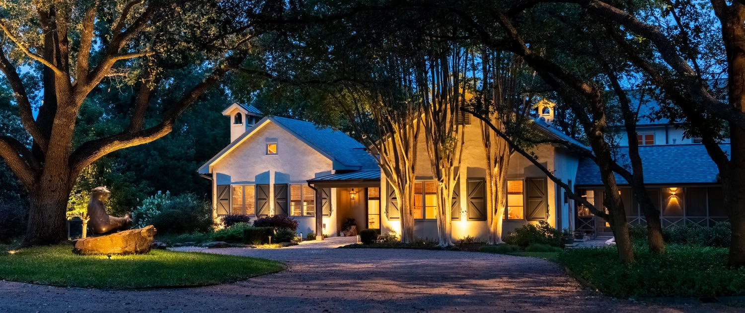 Lumos Outdoor Lighting Residential Exterior Beautifully illuminated house with outdoor lighting highlighting trees and pathway at dusk for enhanced curb appeal and security.