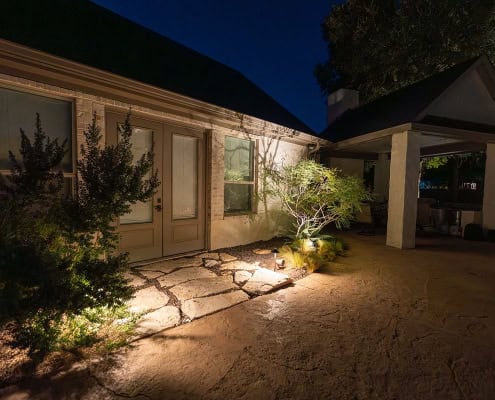 The Poolside Serenity—Moonlit Canopy Design Night view of poolside canopy design, illuminated by landscape lighting. Stone patio leads to French doors, with lush greenery adding to the serene ambiance.