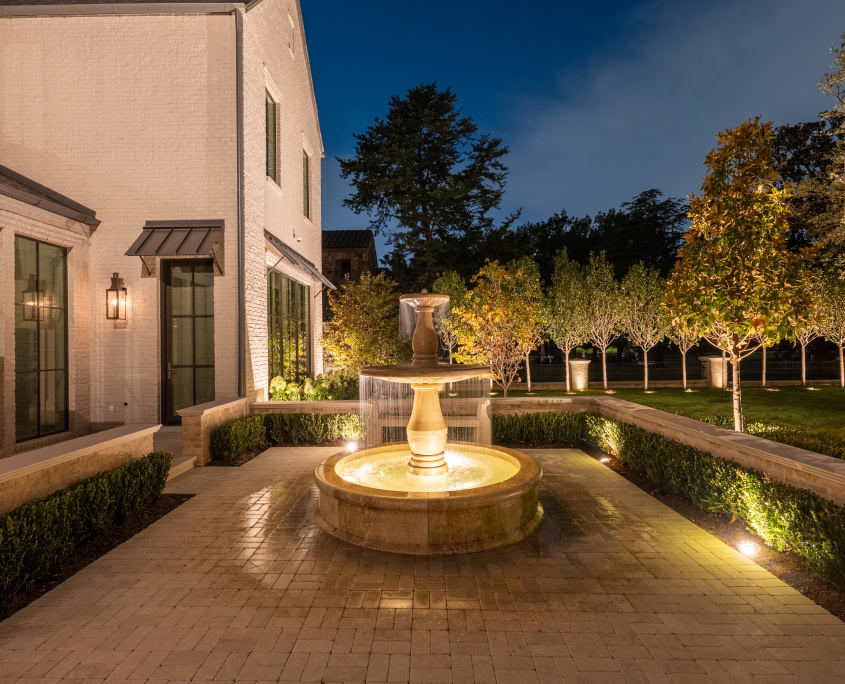 Elegant Outdoor Fountain Lighting Night view of a beautifully illuminated outdoor fountain in a landscaped backyard with trees and pathway lighting.