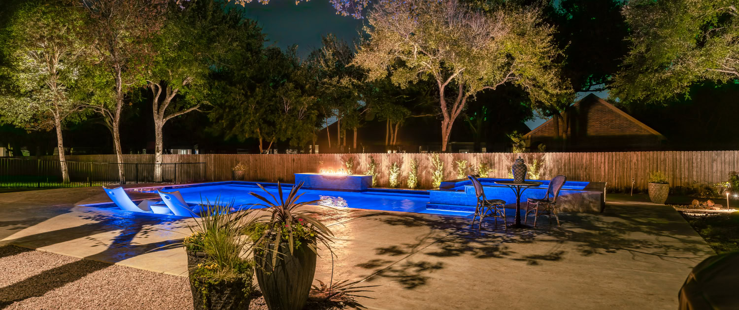 Lumos Outdoor Lighting Pool Area Night view of a backyard with illuminated pool, outdoor seating, and landscape lighting by Lumos Outdoor Lighting.