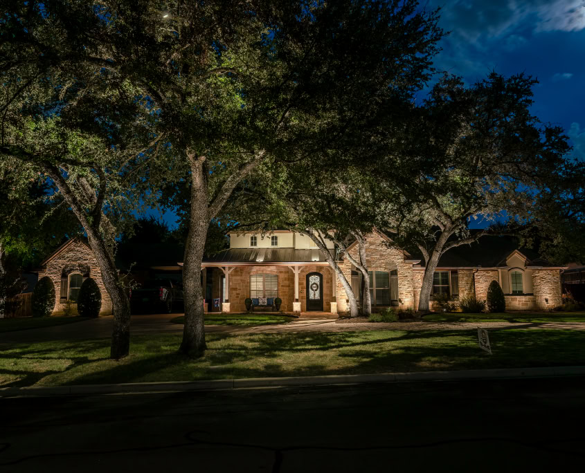 Night view of a residential house illuminated by Lumos Outdoor Lighting, showcasing landscape and pathway lighting for enhanced curb appeal and security.